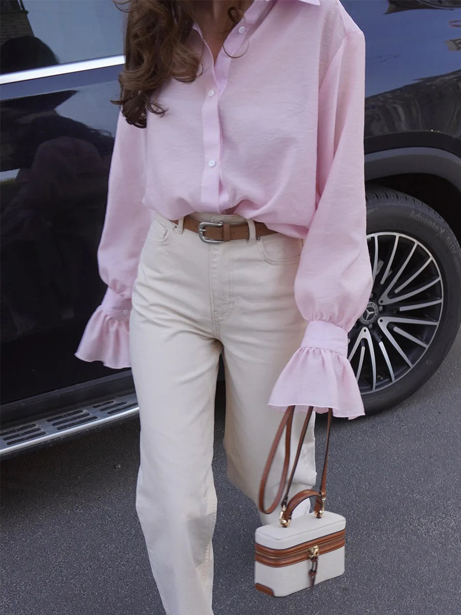 Person wearing a pink blouse and white pants holding a small handbag, standing next to a car.