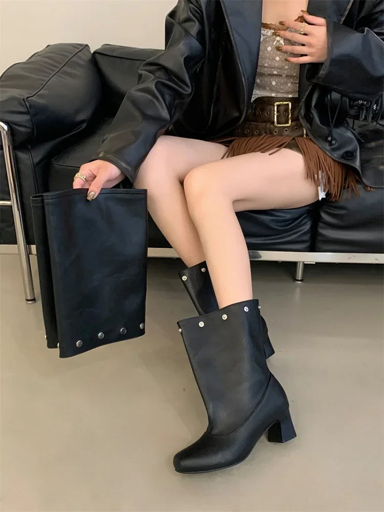 Person wearing black knee-high boots sitting on a black couch holding a black clutch.