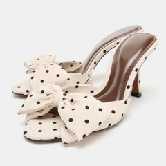 White high-heeled shoes with black polka dots and large bows on a white background