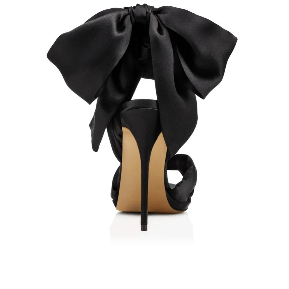 Black high-heeled shoe with a large bow on a white background
