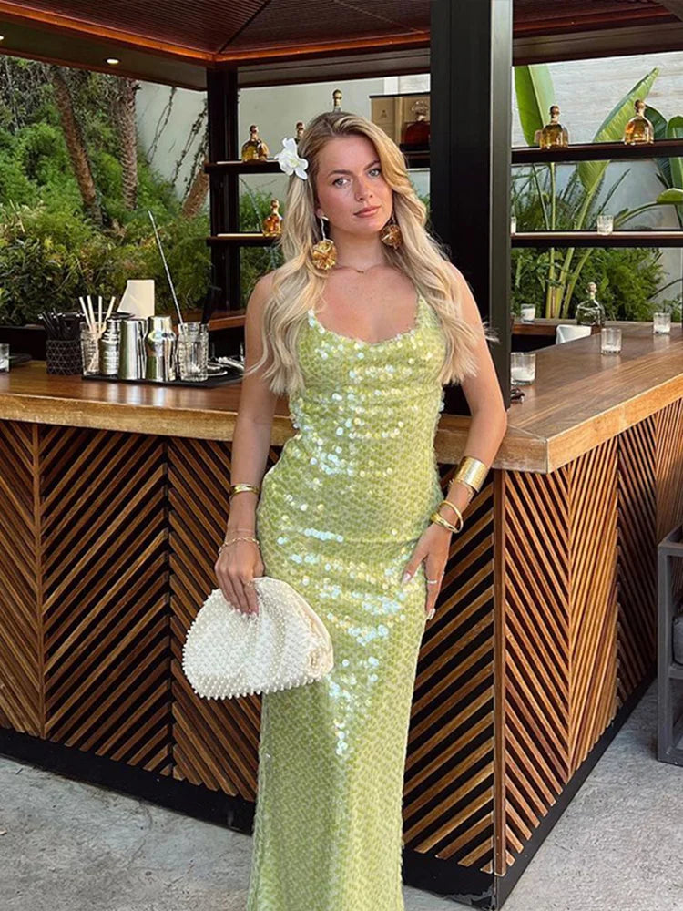Woman in a green sequin dress standing in front of a bar counter.