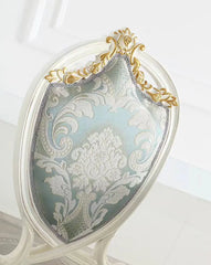 Decorative handbag with intricate gold and silver patterns on a white background