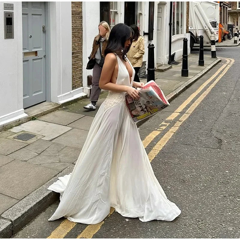 Woman in a white dress reading a magazine on a street.