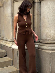 Woman in a brown outfit standing against stone columns.