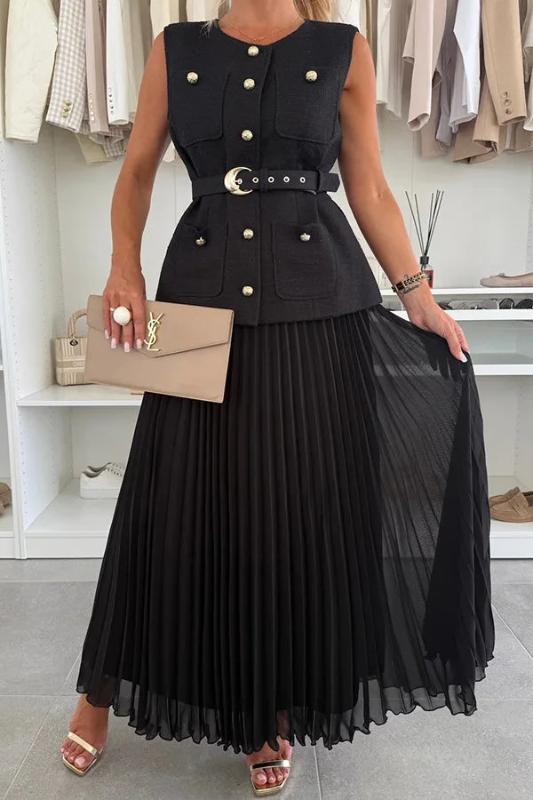 Woman wearing a black sleeveless jacket with gold buttons and a pleated black skirt, holding a beige handbag.