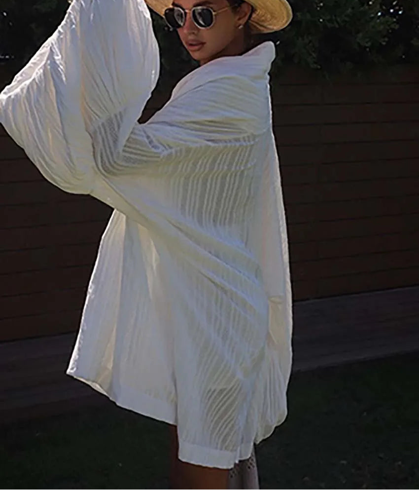 Woman wearing a white cover-up with a straw hat and sunglasses outdoors.