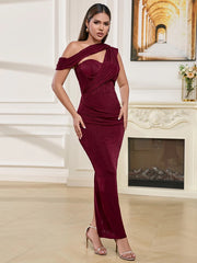 Woman in a burgundy off-shoulder dress standing in a room with a fireplace and painting.