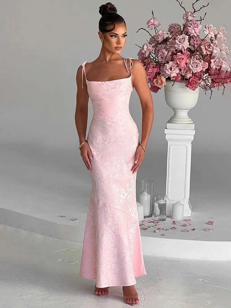 Woman in a pink evening gown standing next to a floral arrangement in a decorative setting.