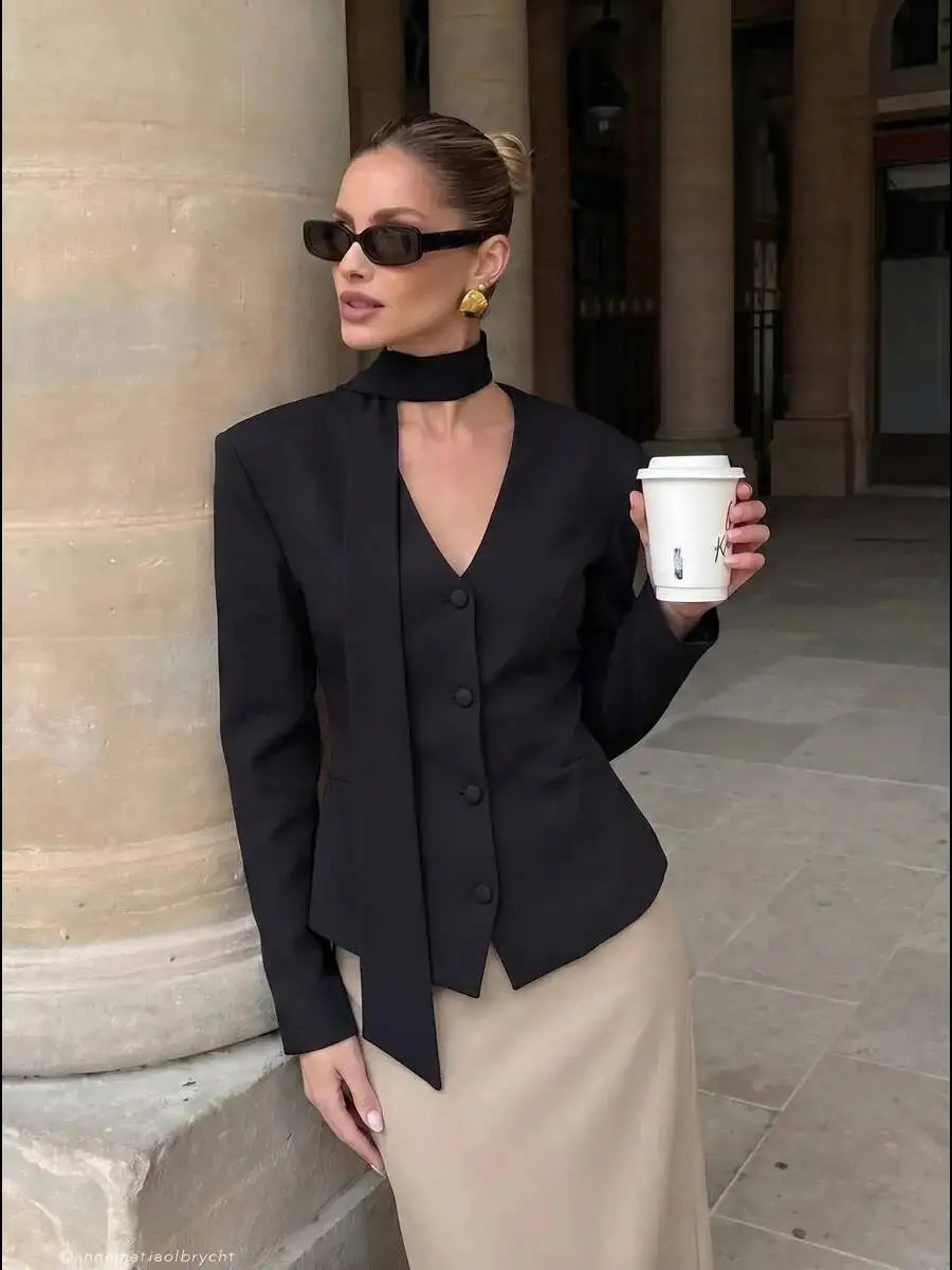 Model wearing a black padded shoulder v-neck blazer with a beige skirt.