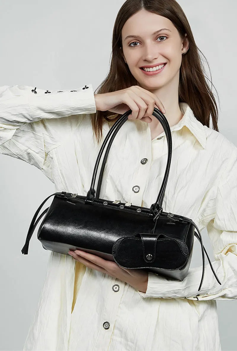 Woman holding a black handbag against a plain background