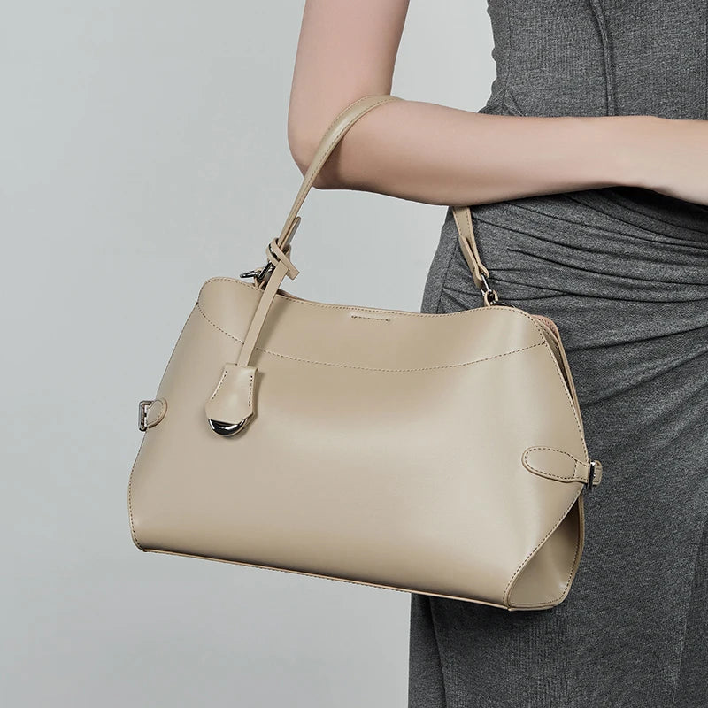Beige handbag held by a person wearing a gray dress on a light gray background