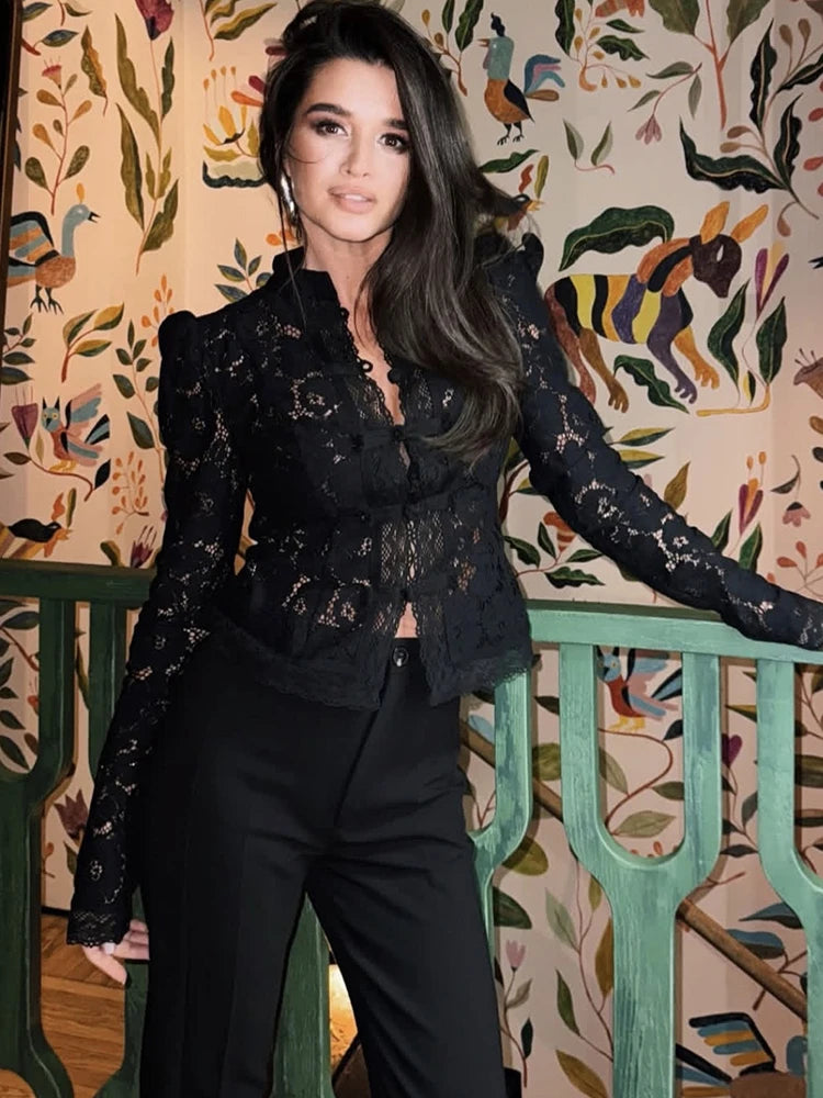 Woman in a black lace outfit standing against a decorative wall with animal illustrations.