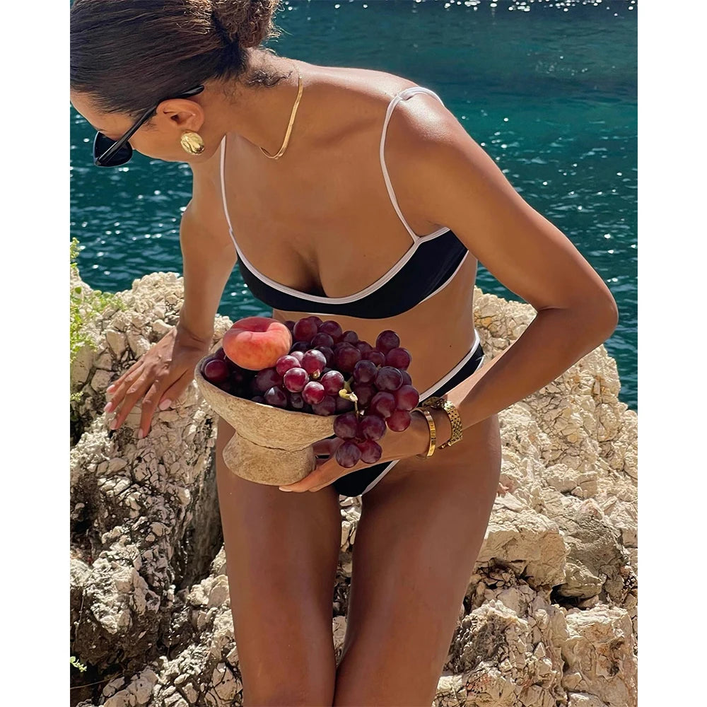 Close-up of a bikini top and bottom with contrast trim, worn by a model on rocks by the sea.