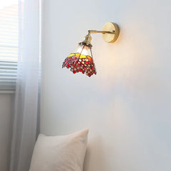 Wall-mounted light fixture with colorful glass shade on a white wall.