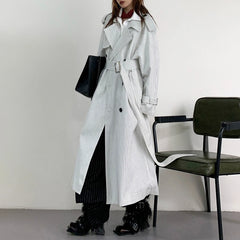 Person wearing a long striped coat standing next to a chair against a plain background