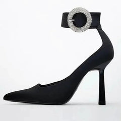 Side view of black pointed toe pump with rhinestone ankle strap buckle.