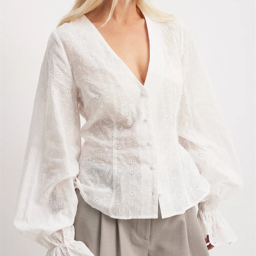 White blouse with long sleeves and floral patterns on a plain background
