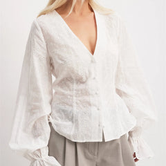 White blouse with long sleeves and floral patterns on a plain background