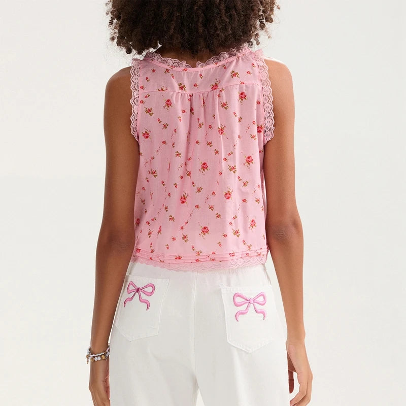 Person wearing a pink floral sleeveless top and white pants with pink bows on a white background