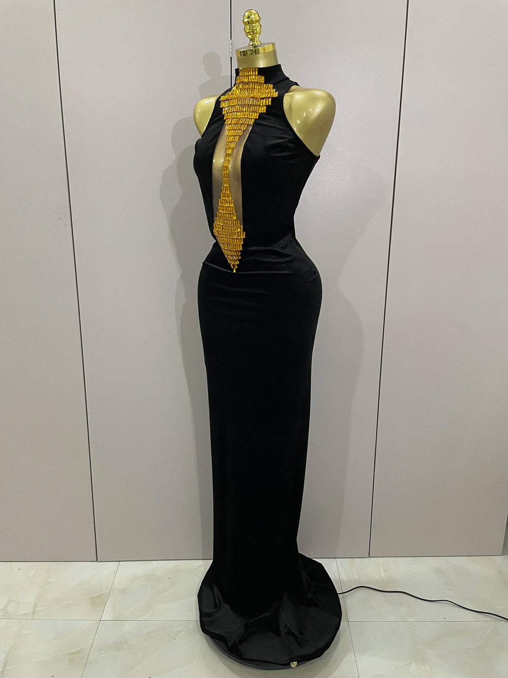 Black evening gown with gold embellishments on a mannequin against a plain background