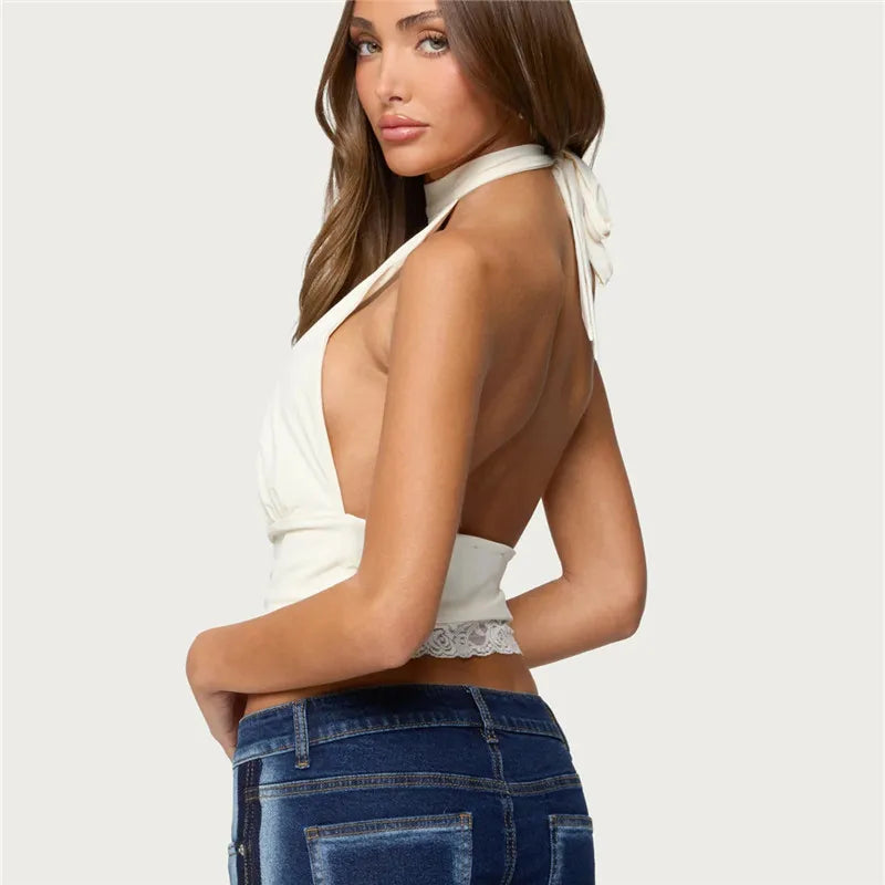 Woman wearing a white top with lace details and blue jeans on a plain background