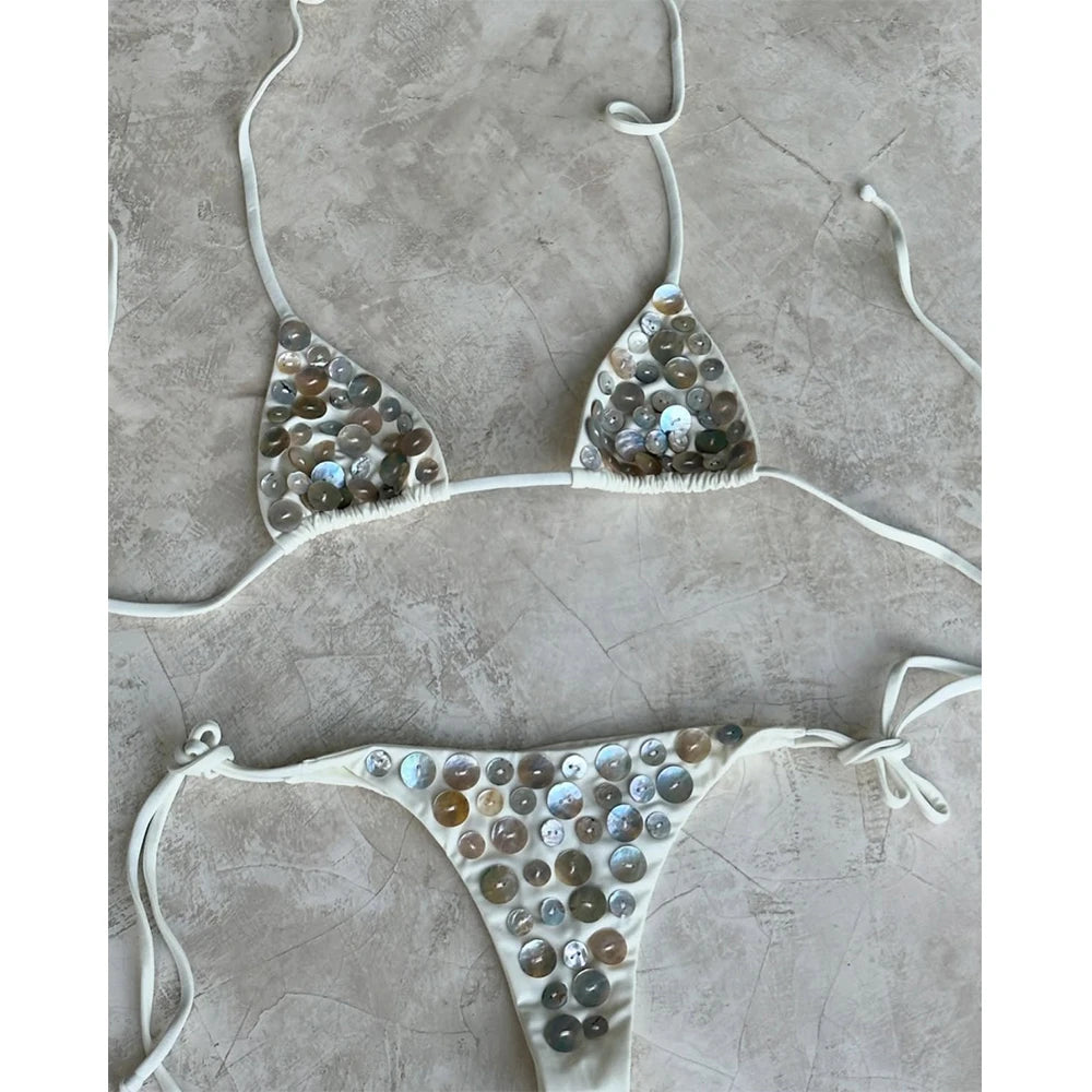 White embellished bikini set on a grey concrete-like surface.