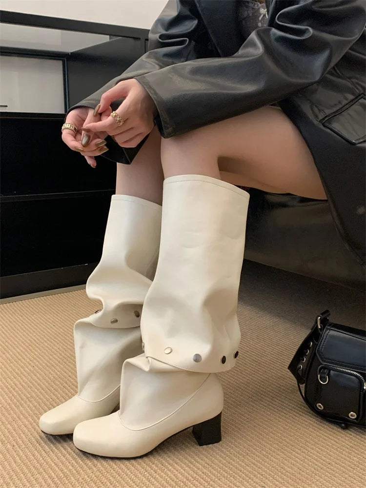 Person wearing white knee-high boots sitting on a couch with a black handbag beside them.