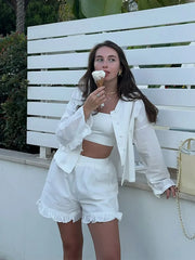 Woman in a white outfit eating ice cream against a white wall with greenery.