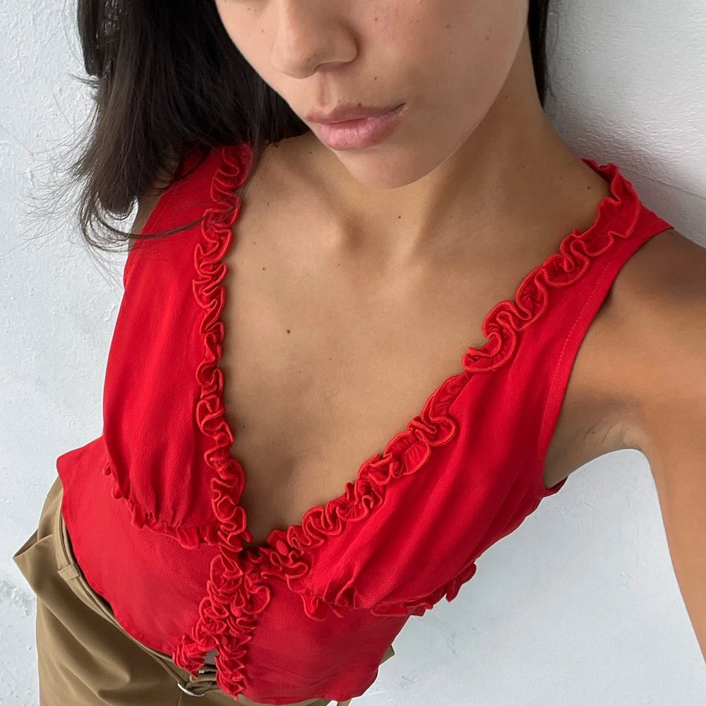 Red ruffled V-neck tank top worn by a woman against a white wall background