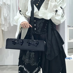 Person holding a black patent leather baguette bag with bow detail