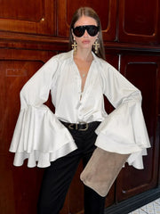 Person wearing a white blouse with ruffled sleeves and black pants in front of wooden cabinets.