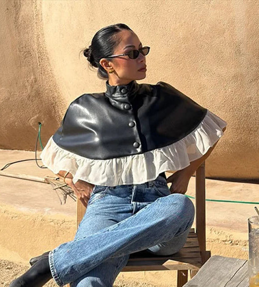 Person sitting outdoors in a desert-like setting wearing a black and white outfit.