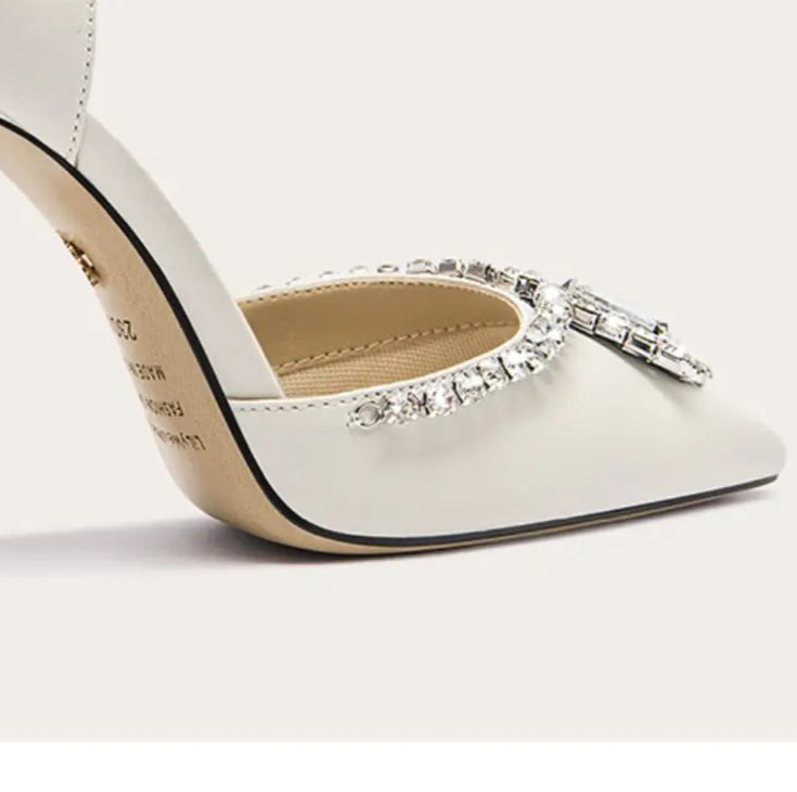 White high-heeled shoe with decorative strap on a light gray background