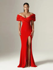 Woman wearing a red off-shoulder gown with a high slit on a plain background