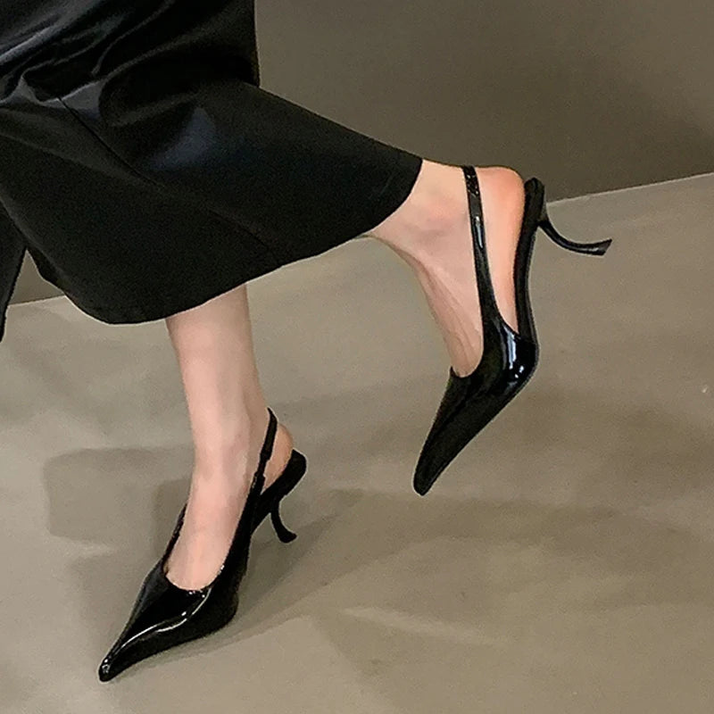 Black patent leather heels worn with black pants on a neutral background