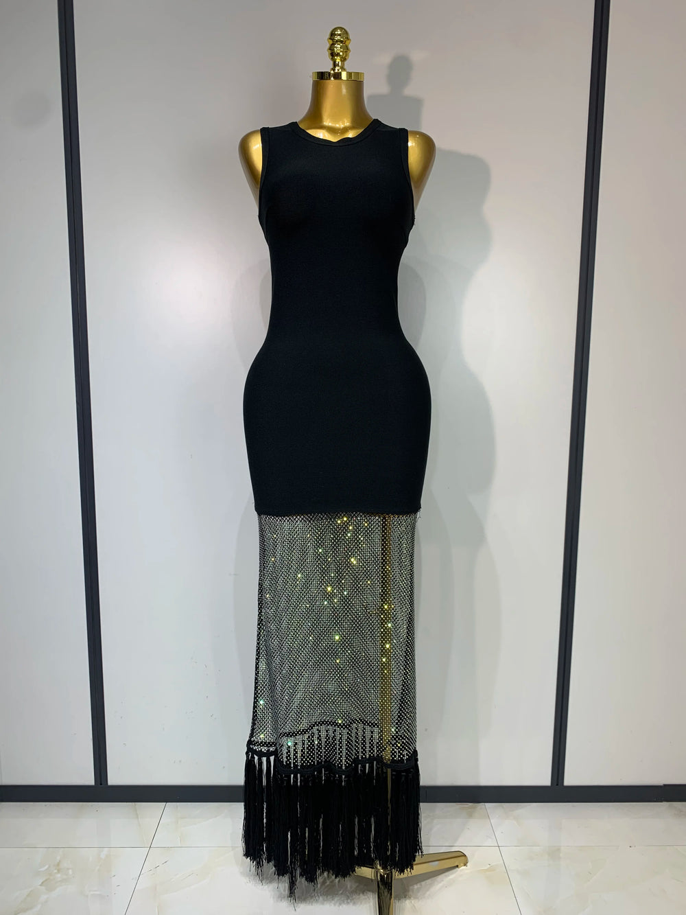 Black dress with a sheer, fringed bottom section on a mannequin against a white background