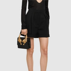 Model holding a black crocodile effect top handle bag with gold tiger sculptures