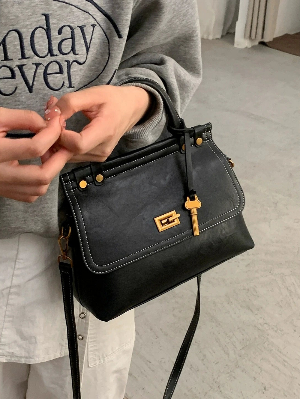 Person holding a black handbag with a gold lock on a light gray floor.