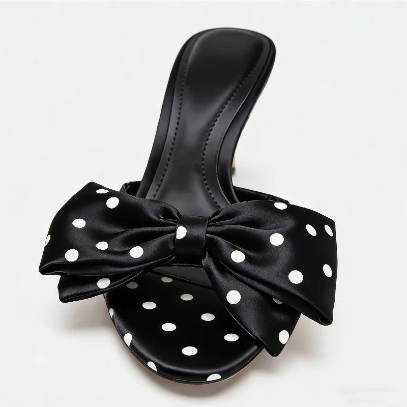 Black sandal with a large bow featuring white polka dots on a light gray background