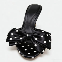 Black sandal with a large bow featuring white polka dots on a light gray background