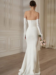 A woman in a white wedding dress with long sleeves holding a bouquet in a room with a wooden floor and white walls.