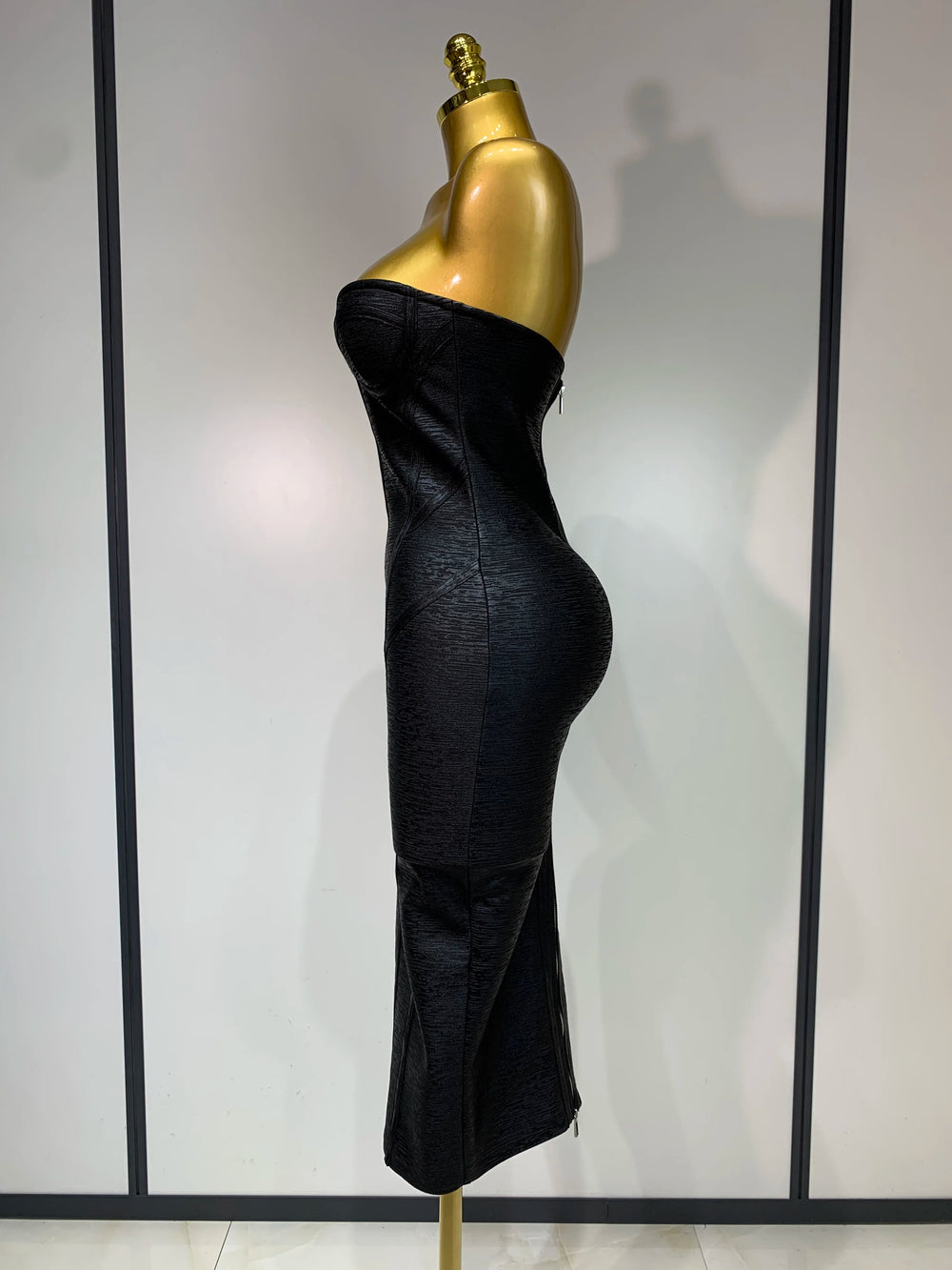 Black strapless dress on a gold mannequin against a neutral background