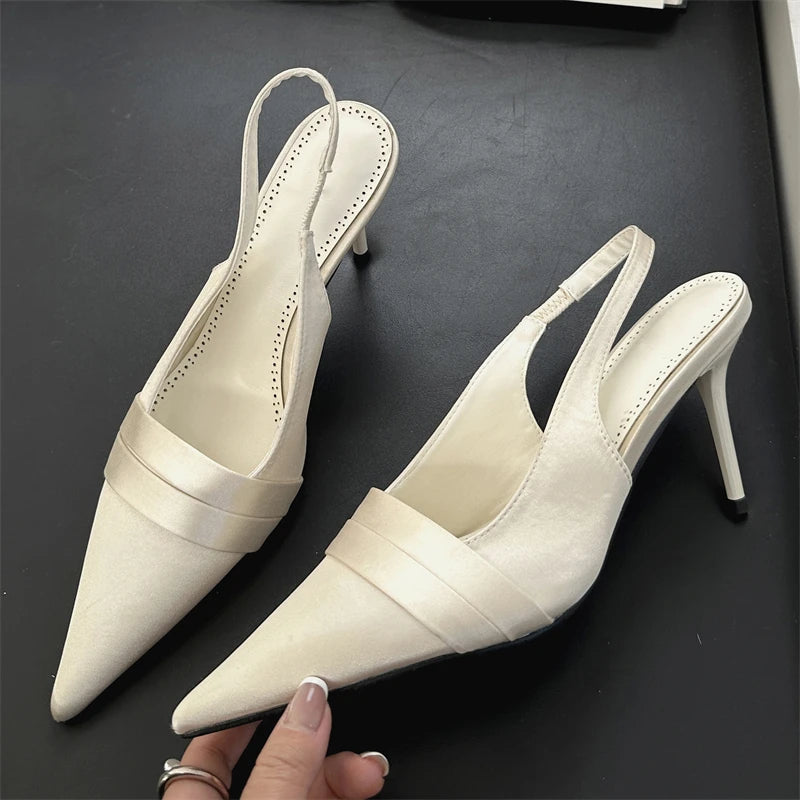 A pair of white heeled shoes on a dark surface with a hand holding one shoe.