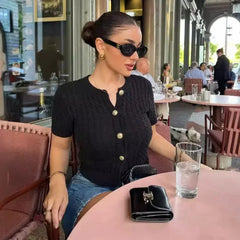 Woman sitting at a table in an outdoor cafe wearing sunglasses and a black top.
