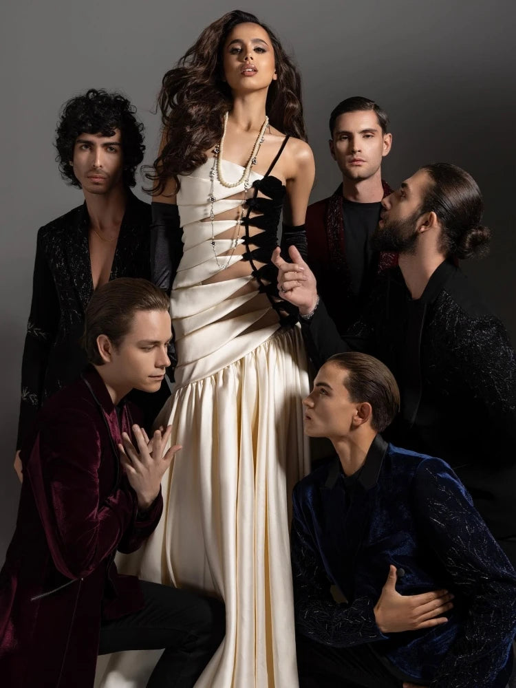 Woman in a white dress surrounded by men in dark clothing against a gray background