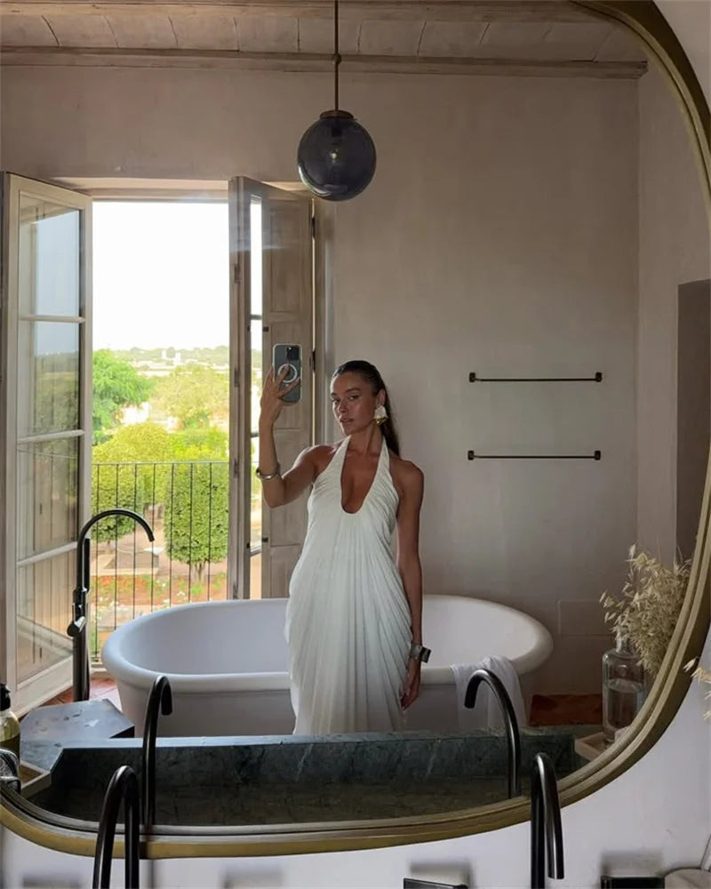 Woman in a white dress taking a mirror selfie in a bathroom with a bathtub and open door.