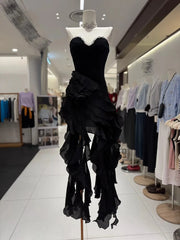 Black ruffled dress on a mannequin in a store setting with other clothing in the background.