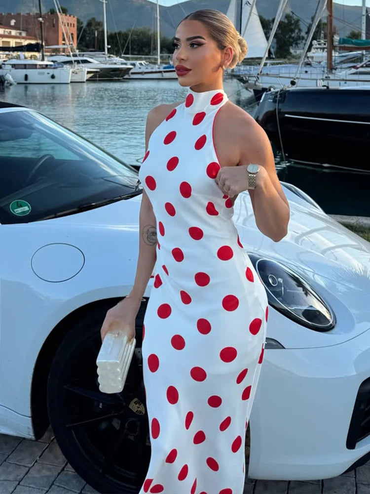 Polka dot halter neck maxi dress standing next to a white car.