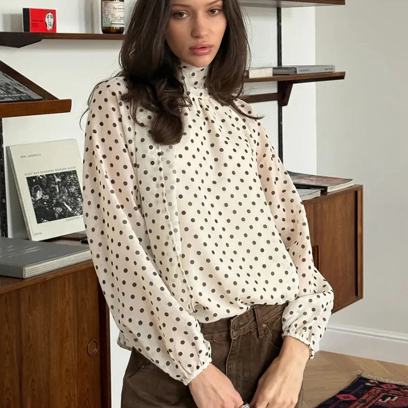 Woman wearing a polka dot blouse in a room with wooden furniture and books.