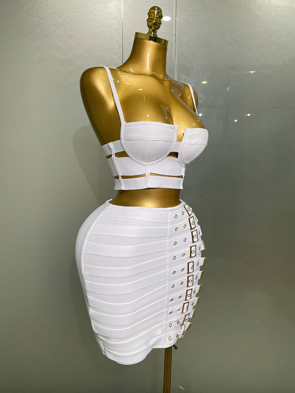 Mannequin wearing a white outfit with gold accents on a plain background